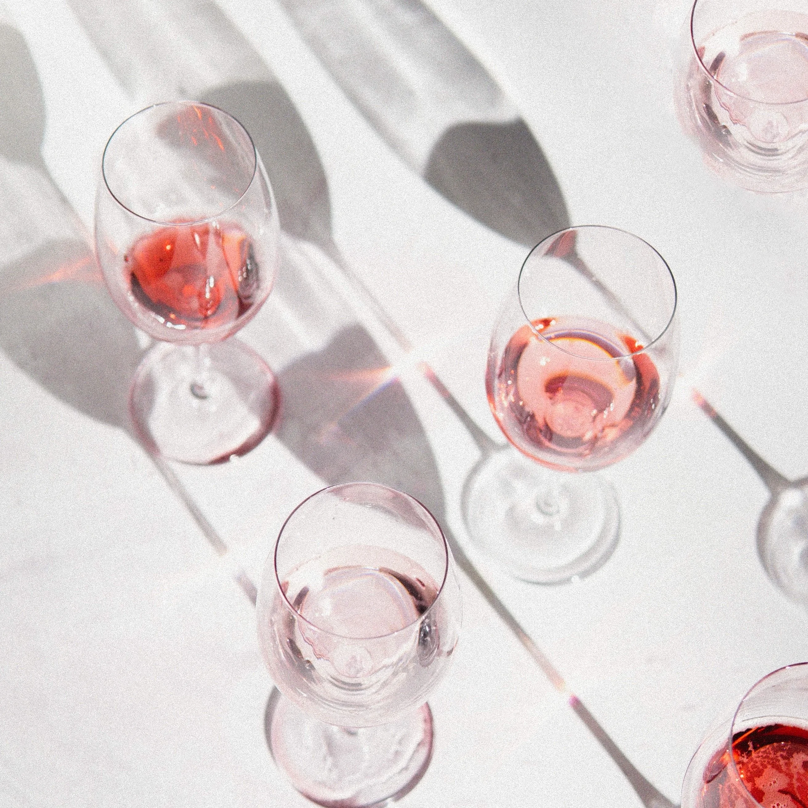 Rose wine in glasses with shadows on a white surface