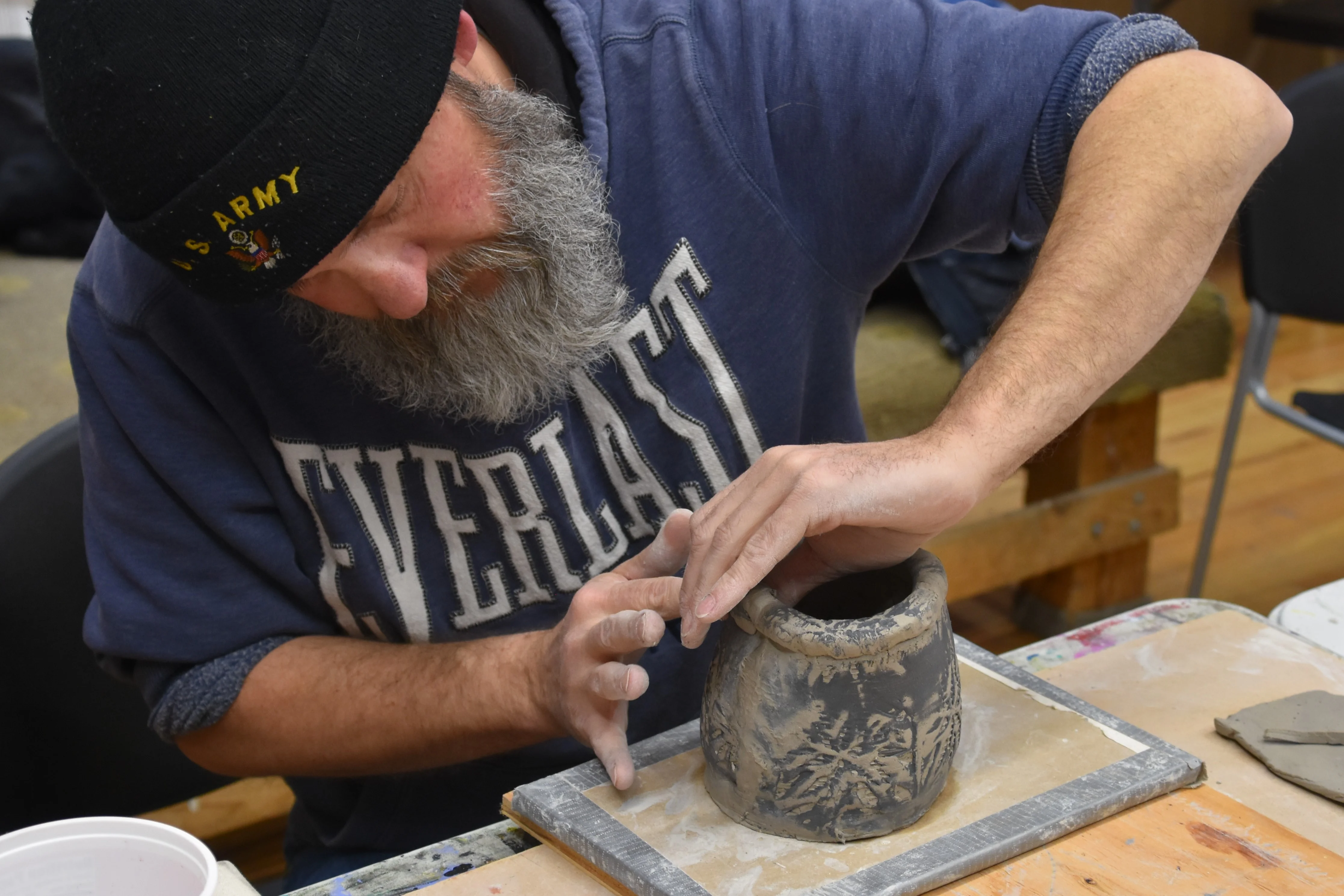 Man with a beanie shaping clay on a potter's wheel.