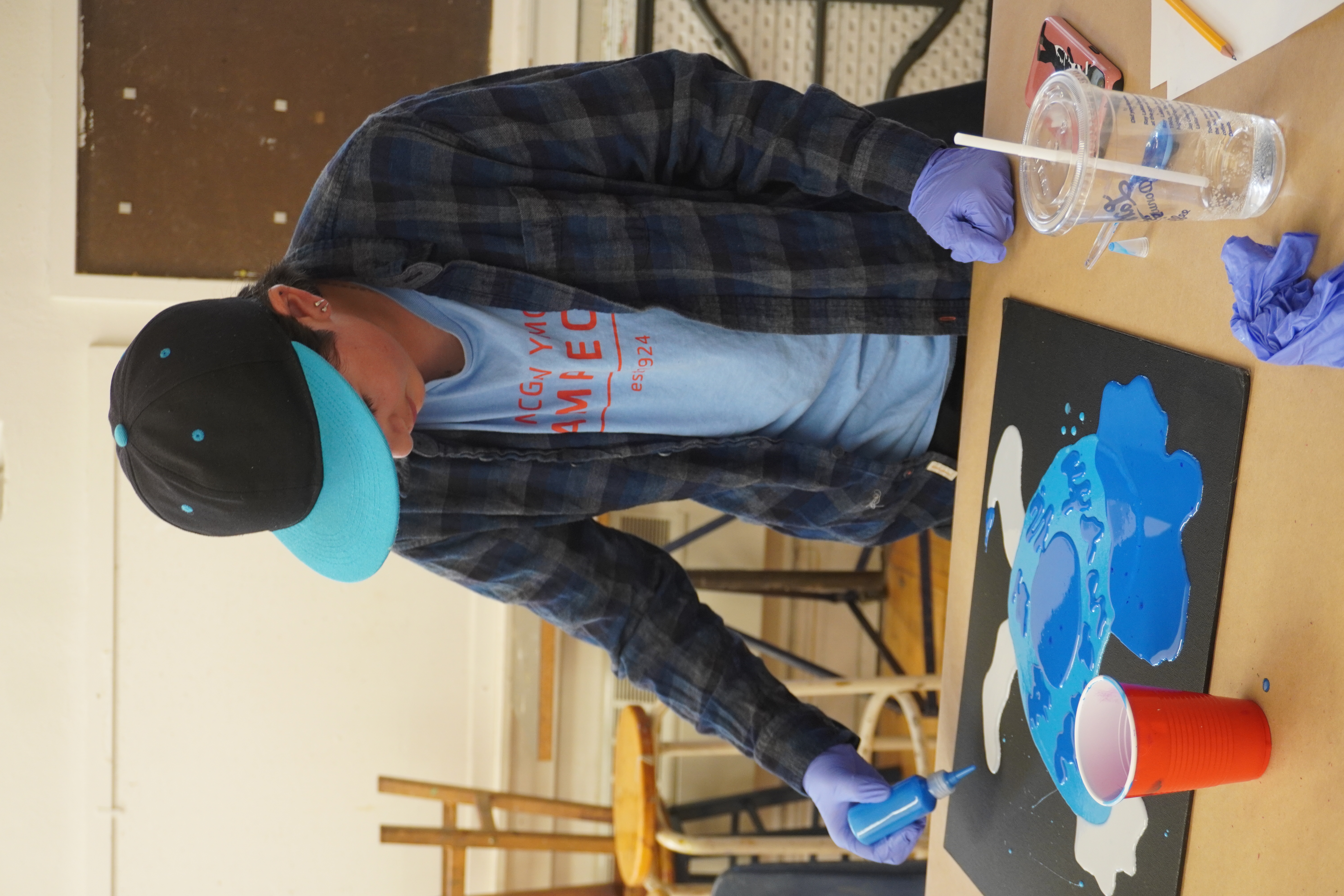 Teen with cap and flannel wearing disposable gloves creating artwork