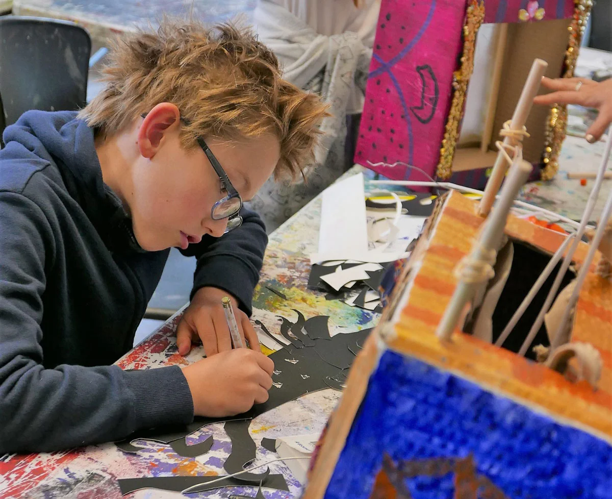 Kid engaged in art and craft activities, surrounded by art supplies.