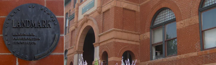 Close-up of a landmark plaque next to a historic brick building with arched entryway and windows.