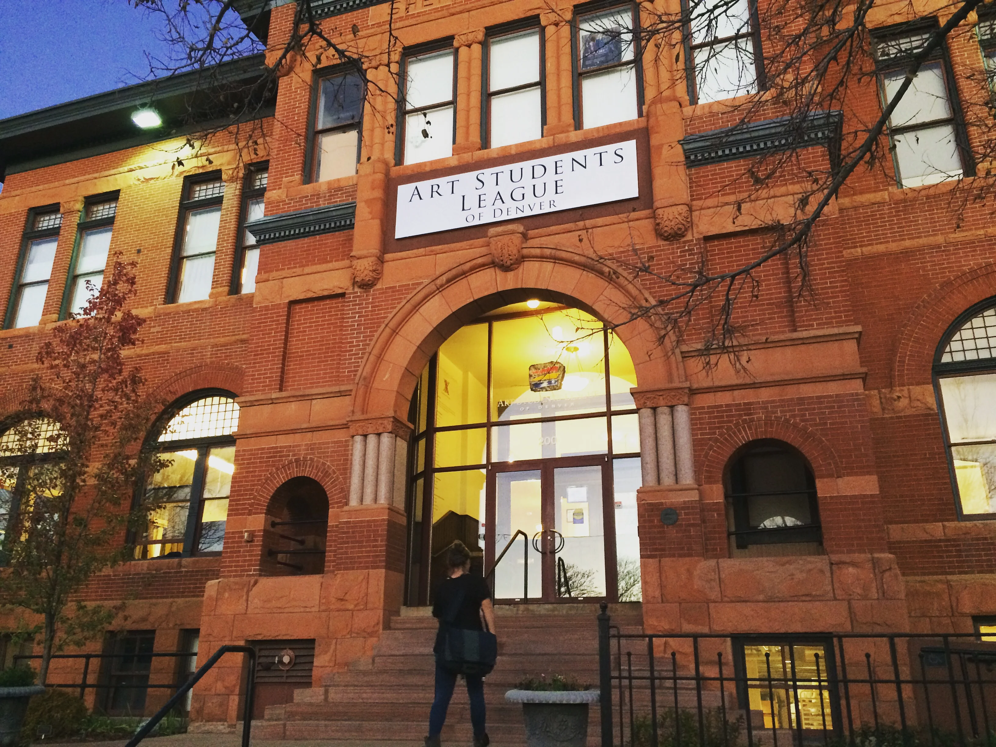 Person walking into the Art Students League of Denver building at dusk.