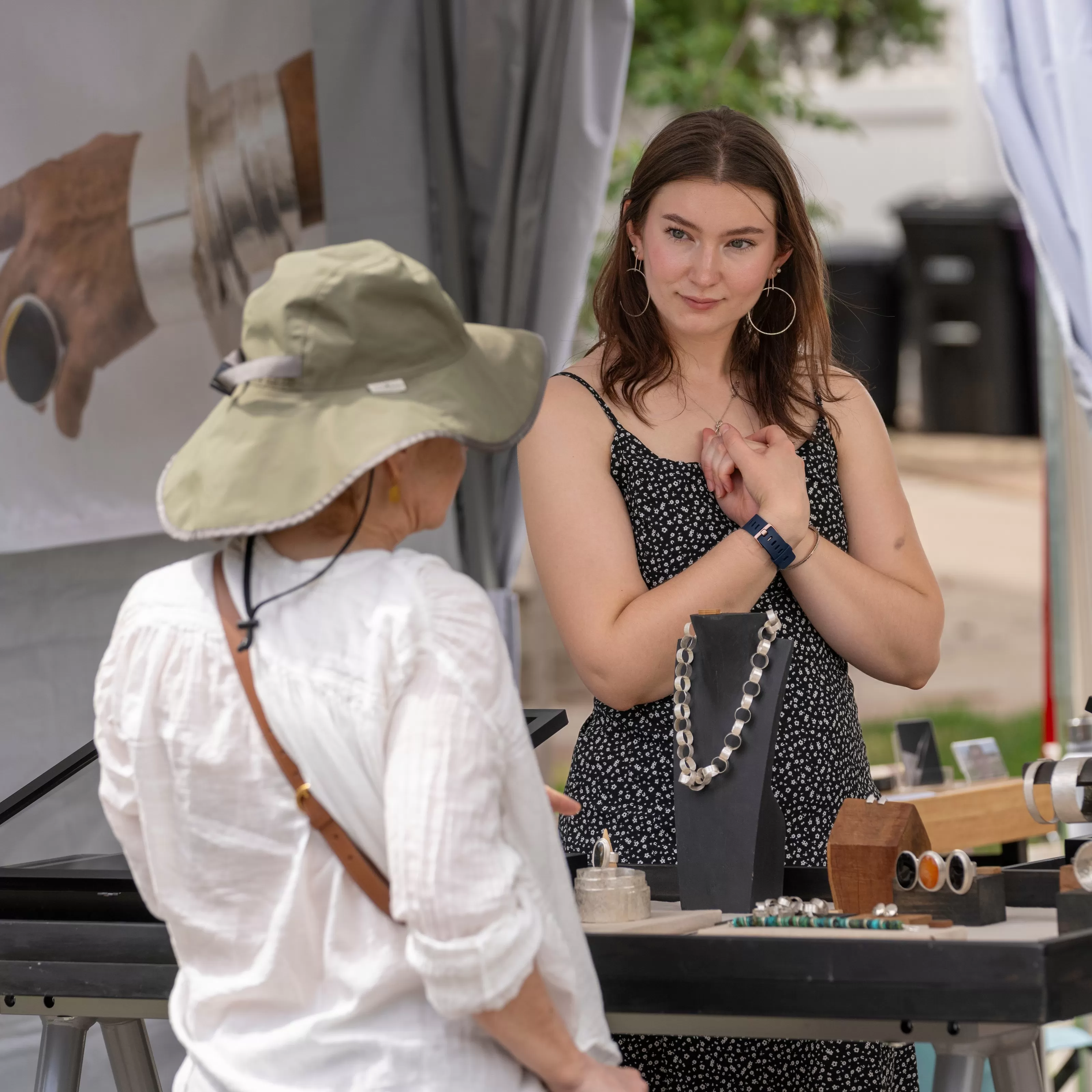 Jewlery artist in her booth interacting with a visitor at Summer Art Market.